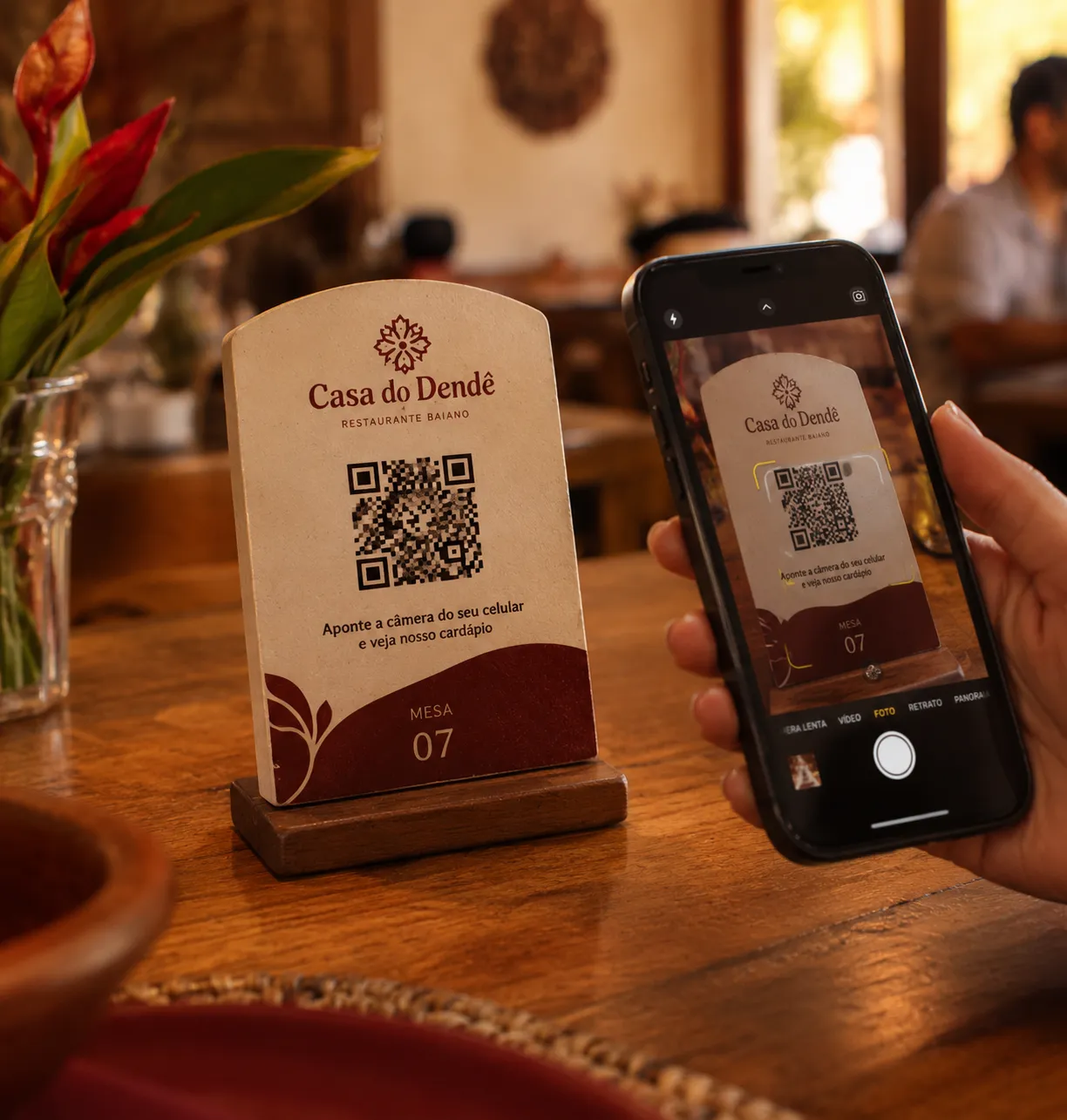 Cliente apontando o celular para o QR Code na mesa do Casa do Dendê, abrindo o cardápio digital.